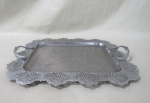 METAL PRATEADO INOX - Bandeja retangular em aço inox, ricamente cinzelado, borda com decoração vazada, alças laterais terminadas em flor, 1 alça solta. Med.: 38x30,5cm.