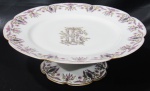 V. TOR ETIENNE, França - Fruteira em porcelana com esmaltagem branca. Borda contornada com raminhos em grisaile e flores em policromia. Centro com monograma "FL", bordas filetadas a ouro com falhas na douração. Marcado no fundo. Medidas: 7,5x22,5cm.