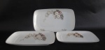 SCHMIDT - Três travessas em porcelana nacional esmaltada na tonalidade branca com pintura de flores e folhagem em policromia e realces em branco, borda filetada a prata com pequenas falhas. Med.: 36x20,5cm / 32,5x18cm / 28x16cm.