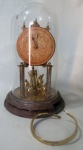 RELÓGIOS - Relógio de mesa alemão MOHERTUS TRADING CO. em metal dourado com base circular em ferro, mostrador com algarismos arábicos e cúpula em vidro com pêndulo solto. No estado. Não testado e sem garantia de funcionamento, Med.: 26cm. C/ CUPULA: 30cm.