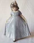 Graciosa escultura de "Menina com vestido azul", em porcelana dinamarquesa, manufatura de Royal Copenhagem, n 2444. Med. 21 x 17 cm. Estimativa R$ 500,00/ R$ 700,00