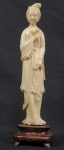 KUAN YIN -  ESCULTURA EM MARFIM REPRESENTANDO FIGURA DE KUAN YIN A DEUSA DA MISERICÓRDIA.  SEGURA NA MÃO DIREITA RAMOS DE PEONIA.  ASSENTE SOBRE BASE EM MADEIRA. CHINA, SEC. XIX. 26 CM DE ALTURA