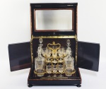 BACCARAT  COM ETIQUETA DA MANUFATURA  PRINCIPESCO TANTALUS EM MADEIRA COM CRISTAL BIZOTADO ESTILO E ÉPOCA NAPOLEÃO III. CONSTRUÍDO COM MADEIRAS EXÓTICAS E PRECIOSAS ACOMODA EM SEU INTERIOR SUPORTE EM BRONZE ORMOLU ONDE SE ENCAIXAM QUATRO LINDAS LICOREIRAS VIRTUOSAMENTE LAPIDADAS COM ÁRVORES, PÁSSAROS, MARIPOSAS, VEGETAÇÃO LACUSTRE  E 14 CÁLICES DO TIPO CORDIAL COM A MESMA LAPIDAÇÃO. RARA PRESENÇA DE ETIQUETAS DA MANUFATURA DE BACCARAT EM PAPEL COMO ERAM NO PERÍODO ANTERIOR A DEC. 1930. DIFICILMENTE ENCONTRADAS PORQUE AO SEREM LAVADAS AS PEÇAS A ETIQUETA SIMPLESMENTE ERA ELIMINADA. O SUPORTE EM BRONZE ORMOLU É REMATADO POR FLORES E ROCAILLES. DIFICILMENTE SE VERÁ UM CONJUNTO DE TANTALUS NAPOLEÃO III EM TAL EXCEPCIONAL ESTADO DE CONSERVAÇÃO E BELEZA. FRANÇA, SEGUNDA METADE DO SEC. XIX. 28 X 34 X 25 CMNOTA: O nome Tantalus faz referencia ao personagem da mitologia Grega Tântalo, rei da Frígia e filho de Zeus com a princesa Plota. Certa vez por ser filho do Rei de Zeus, foi admitido na mesa dos deuses, ouviu seus segredos, e divulgou entre os mortais, sendo punido por isso. Seu castigo foi ser lançado ao Tártaro, onde, num vale abundante em vegetação e água, foi sentenciado a não poder saciar sua fome e sede, visto que, ao aproximar-se da água esta escoava e ao erguer-se para colher os frutos das árvores, os ramos moviam-se para longe de seu alcance sob a força do vento. A expressão suplício de Tântalo refere-se ao sofrimento daquele que deseja algo aparentemente próximo, porém, inalcançável, a exemplo do ditado popular "Tão perto e, ainda assim, tão longe". Assim trancados no tantalus as bebidas ficavam a salvo de empregados e de crianças.