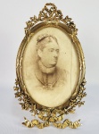 DONA VERIDIANA DA SILVA PRADO - RETRATO DE DONA VERIDIANA VALÉRIA DA SILVA PRADO PINTADO SOBRE GALALITE A PARTIR DE FOTOGRAFIA. ACONDIONADO EM PORTA RETRATOS EM BRONZE ORMOLU  DE FINA FUNDIÇÃO ESTILO IMPÉRIO.  ASSINADO PELO ARTISTA. FINAL DO SEC. XIX. 17,5 CM DE ALTURANOTA: Veridiana Valéria da Silva Prado (São Paulo, 11 de fevereiro de 1825  São Paulo, 11 de junho de 1910) foi uma aristocrata, proprietária de terras, que, loteadas no processo de industrialização da cidade de São Paulo durante o século XX, compreendem hoje bairros paulistanos inteiros, e intelectual brasileira. Mulher poderosa da alta sociedade, marcou profundamente a vida social, política e cultural de São Paulo no final do Império e início da República Velha. Administrou as fazendas da Família Prado, uma importante família que desde o século XVIII comercializava escravos e açúcar, e comandou em sua Chácara Vila Maria um dos salões culturais de maior importância de São Paulo na segunda metade do século XIX, que posteriormente ficou conhecido como o Palacete de Dona Veridiana.56 Lá recebeu artistas, intelectuais, cientistas, estadistas e membros da Família Real como D.Pedro II e a Princesa Isabel. Foi uma mulher marcante para a cidade, seja pelas obras de caridade, ou pelo seu incentivo à agricultura, aos esportes e às artes. Também destacou-se devido aos seus empreendimentos, sendo inclusive proprietária do jornal O Comércio de São Paulo e dona de fazendas e casas comerciais de café. Era filha de Antônio da Silva Prado, barão de Iguape, cafeicultor, comerciante de açúcar e de tropas, um dos paulistanos mais ricos da época, e de Maria Cândida de Moura Vaz. Os seus pais enfrentaram preconceito social e uma barreira legal ao casarem-se, pois a mãe, Maria Cândida, era uma mulher divorciada. Veridiana casou-se com seu meio-tio Martinho da Silva Prado, mas depois separou-se, sendo o divórcio considerado um escândalo para a sociedade da época. No entanto, ela obteve o comando da família e teve 6 filhos, 36 netos e 96 bisnetos. Veridiana educou os filhos, que exerceram papéis de destaque na política, nos negócios, na vida social e cultural do país, entre eles, Antônio da Silva Prado, seu filho primogênito, que foi Ministro de Estado, senador, deputado e o primeiro prefeito de São Paulo ( 1899 a 1911) e Eduardo Prado, fundador da Academia Brasileira de Letras.Atualmente possui uma rua em sua homenagem, a Rua Dona Veridiana, localizada no bairro de Higienópolis, em São Paulo. Veridiana nasceu na propriedade do pai, em São Paulo, no dia 11 de fevereiro de 1825, no casarão de sua família, que ficava até então na Rua Direita, esquina com a Rua São Bento, na atual Praça do Patricarca. Ela tinha um irmão mais velho chamado Veríssimo e não houve distinção na criação dos dois, pois o pai deles não queria criar a filha para que ela se tornasse submissa ao marido. O barão de Iguape desejava que Veridiana seguisse os passos da mãe e da avó, Ana Vicência, que eram mulheres poderosas da Família Prado, empreendedoras e carismáticas. Na casa da família, três anos antes do nascimento de Veridiana, o seu pai, Antônio da Silva Prado, hospedara o príncipe regente Dom Pedro I, em 1822, ano em que o monarca visitou São Paulo, e proclamou a independência do Brasil. Antônio Prado já era homem rico, sobretudo por conta de uma fortuna que vinha das tropas de mulas e do comércio. Veridiana podia escutar as conversas das personalidades que visitaram o casarão na Rua Direita, entre eles, estadistas, artistas, cientistas e homens de negócios, que conversavam sobre empreendimentos, alianças políticas e questões municipais como a construção do teatro São José e da Santa Casa de Misericórdia. Antônio Prado, em uma de suas viagens de negócios ao Rio de Janeiro, levou os filhos para conhecer a Corte. Foram recebidos pela Marquesa de Santos, amante do imperador e a mulher mais influente da Corte. Na infância, Veridiana se destacava diante a todos devido à graça e à vivacidade. A Marquesa teria a elogiado, ao chamá-la de menina misureira. Veríssimo e Veridiana foram apresentados a Daniel Müller, um engenheiro da época muito conhecido, que teria fascinado as crianças com suas explicações sobre edificações de palácios, demonstrando uma enorme curiosidade de Veridiana desde cedo. Durante o período da Regência, a menina estudou, leu, viajou com os pais e aprendeu inglês, francês e alemão com suas governantas. Era muito interessada - de bonecas e livros aos negócios do pai. No dia 24 de junho do ano de 1838, completando 13 anos, por imposição paterna, Veridiana casou-se com seu meio-tio Martinho da Silva Prado, quatorze anos mais velho do que ela. Seu casamento precoce com o próprio tio foi uma forma de proteção ao patrimônio da família. O casamento foi discreto e ocorreu no oratório do bispo D.José Antônio dos Reis, no Rio de Janeiro Dois meses depois, o ex-marido da mãe de Veridiana, Maria Cândida, faleceu e houve a legalização do casamento dos pais de Veridiana, que foi realizado na casa do barão de Iguape, no dia 10 de agosto de 1838. O primeiro filho de Veridiana nasceu quando ela tinha 15 anos. Aos 22, ela já era mãe de cinco filhos, e até os 35 anos de idade, teve mais outros três filhos.No entanto, nem todos sobreviveram, morrendo duas meninas. Durante os 10 primeiros anos de casamento, ela viveu com o marido Martinho na recém-adquirida Fazenda Campo Alto, que ficava então em Mogi Mirim. 1839 foi o ano em que o casal conseguiu mudar-se para a fazenda, que era um grande engenho produtor de açúcar, já que no início do século XIX o café não era uma cultura importante em São Paulo. Veridiana ajudou Martinho a comprar Campo Alto com a venda de suas jóias, sendo sócia do marido nos negócios. Ele, por outro lado, fez muita economia e mesmo sendo um homem que gostasse de ir à festas, deixou de ir, pois não tinha roupas. A propriedade tornou-se uma fazenda-modelo de produtividade e rentabilidade e o casal só a deixava para ir a São Paulo quando Veridiana estava para dar à luz. Quando em São Paulo, o casal ficava em uma chácara na Consolação, que era uma propriedade auto-suficiente. Apesar da convivência feliz entre Veridiana e Martinho, as diferenças pioraram entre eles especialmente após a morte do Barão de Iguape, em 1875, que era um grande mediador nos conflitos familiares. No ano de 1876, a filha do casal, Ana Blandina, solteira e com 33 anos, é pedida em casamento por Antonio Pereira Pinto Júnior. Veridiana aceita a proposta, mas Martinho se opõe. Veridiana ganha pela insistência e o casamento ocorre em março de 1877. Mas, a relação entre Veridiana e Martinho se desgasta e eles se separam em 1878. O divórcio era considerado um escândalo para a elite paulista da época. No entanto, Veridiana nunca se separou legalmente, apenas viveu uma vida paralela ao ex-marido. O vínculo formal ainda foi mantido com Martinho, que aparece inclusive no testamento de Veridiana, documento produzido em 1884. eridiana ocupava, em 1848, uma chácara ao lado da igreja da Consolação. Mas em 1882, ela viaja para Paris para visitar sua filha Ana Blandina, futura condessa Pereira Pinto pela Santa Sé, que vivia na França com seu marido diplomata. Encantada com a vida intelectual e social em Paris, Veridiana volta para São Paulo e no mesmo ano de 1882 começa a construção de um palacete na chácara que comprara em 1879 no então bairro de Santa Cecília. A chácara fica conhecida como Vila Maria, uma homenagem de Veridiana à sua dama de companhia, Maria das Dores, mulher casada com Antonio Pacheco Chaves, em um matrimônio auxiliado por Veridiana. Na chácara, transformou sua casa em um palacete, um dos locais mais elegantes da cidade e um ponto de encontro para intelectuais, políticos, artistas e cientistas. Veridiana era muito culta, falava bem francês e um pouco de italiano e ainda lia bem nas duas línguas. Em sua propriedade, na Chácara Vila Maria, chegou a receber D.Pedro II (1886), a Princesa Isabel (1884), Orville Derby e Loefgreen, Domingos José Nogueira Jaguaribe, Luis Pereira Barreto, Cesário Motta Junior, Diogo de Faria, além de Capistrano de Abreu, Ramalho Ortigão, Graça Aranha, conde D'Eu, Teodoro Sampaio, Joaquim Nabuco e os negros abolicionistas Luís Gama e José do Patrocínio. Veridiana ainda viveu no mesmo tempo da Rainha Vitória, com a qual era comparada devido a personalidade similar. De acordo com notícia publicada no jornal Correio Paulistano de 19 de novembro de 1884, em seu diário, escreveu a Princesa Isabel: A propriedade de D. Veridiana, lindíssima; casa à francesa, exterior e interior muitíssimo bonitos, de muito bom gosto. Os jardins tem gramados dignos da Inglaterra, a casa domina tudo, há um lagozinho, plantações de rosas e cravos, lindos. Vim de lá encantada. Em seu palacete, onde movimentou sua vida social, Veridiana teve empregados de origens diversas, entre eles, um índio e dois afrodescendentes, sendo que ela tinha como dama de companhia uma jovem negra, que era pianista e só falava com ela em francês. O seu mordomo era um índio botocudo e Veridiana tinha ainda como cocheiro um homem suíço, que a levava a passear de coche durante os fins de tarde pela atual Avenida Higienópolis. Os jardineiros do seu palacete eram todos europeus e ela abria o jardim às crianças do bairro, seguindo o exemplo seguido da condessa Penteado. Vítima de críticas vindas das mulheres da elite paulista, Veridiana ainda teria sofrido um boato de que em seu palacete supostamente ficaria um clube masculino, do tipo dos clubes exclusivos ingleses, sendo o local vedado o acesso de mulheres. Mas essa fabulação popular tem sido refutada como fruto de devaneios dos afortunados na cidade, distanciados da vida comum dos demais moradores de São Paulo. Apesar de Veridiana ser monarquista, mesmo após a Proclamação da República, defendeu a libertação dos escravos.Em 1870 foi presidente da Sociedade Redentora para libertação dos escravos, formada por senhoras da sociedade. Em 1892, para ajudar seu filho caçula, Eduardo Prado, que era dono do jornal O Comércio de São Paulo, Veridiana investiu capital e assumiu a frente do jornal, inclusive em 1902 chegou a requerer na Junta Comercial de São Paulo o registro de uma nova marca para o periódico. Ela depois vendeu o jornal a Francisco Glicério. Em 1901, durante o pico de uma das maiores crises do setor cafeeiro, Veridiana, junto a seu filho Eduardo da Silva Prado, abriu um negócio de compra e venda de "fazendas, secos, molhados, calçados e outros artigos" na Fazenda Brejão, que ficava no município paulista de Santa Cruz das Palmeiras e era um terreno com mais de 730.000 pés de café. Enquanto Eduardo foi para a Europa, em 1881, Verdiana ajudou um dos amigos dele, o geólogo americano Orville Derby, que ficou hospedado na Chácara Vila Maria, onde recebeu cuidados médicos até se restabelecer. Em 1879, Veridiana adquiriu o terreno onde veio a construir seu palacete, com planta em estilo europeu francês, e com material totalmente importado da Europa, ocupando uma grande área, desde a antiga Rua de Santa Cecília (atual Rua Dona Veridiana) até a atual Avenida Angélica, com divisa entre a avenida Higienópolis e a atual Rua Martinico Prado. A propriedade, com belos jardins, pomar, espelho dágua com cisnes e marrecos e cocheiras com cavalos de raça, recebeu o nome de Chácara Vila Maria. A construção ficou a cargo do engenheiro Luiz Liberal Pinto, que foi também o responsável por importar todo o material utilizado. O palacete de Dona Veridiana impressionava os paulistanos mesmo durante as obras que seguiam em 1883. O imóvel, cuja construção foi finalizada em 1884, representa o padrão de ocupação de vila suburbana da virada do Século XIX na cidade de São Paulo. A estrutura do edifício é eclética, algo característico da elite paulistana da época. O local, que constitui marco de origem do bairro de Higienópolis, mistura elementos da Renascença Francesa e possui algumas reminiscências renascentistas italianas. Foi o filho de Veridiana, Eduardo Prado quem a indicou o francês Auguste Glaziou para a criação dos jardins da residência. Conta-se inclusive que o eucalipto foi uma árvore introduzida em São Paulo por iniciativa de D.Veridiana. O palacete possuía também modernos equipamentos, como um aparelho telefônico, cuja instalação ocorrera em 1884. Nessa data, São Paulo tinha apenas onze linhas, sendo Veridiana a única mulher assinante. O palacete era decorado com móveis e peças trazidos de viagens, obras de arte do exterior ou encomendadas a artistas brasileiros como Almeida Junior e Victor Brecheret. O que restou da área do palacete de Dona Veridiana construído em 1884, já abrigou o Velódromo Veridiana Prado, selado após a morte de Veridiana. O que sobrou do terreno também abrigou o São Paulo Clube, que encerrou suas atividades em 2007. O Clube Athletico Paulistano foi inclusive fundado pelos filhos de Veridiana, Antonio e Martinho Prado. Em 1906, seu filho Eduardo Prado teve problemas políticos, correndo risco de ser preso. Veridiana, preocupada, chamara dois ingleses para que a ajudassem a tirar o filho do Brasil. Eduardo, acompanhado pelos dois ingleses até o embarque em Santos, supostamente se passou por padre e viajou para a Europa como Capelão de Bordo em um navio rumo a Southampton. O filho então retornou ao Brasil alguns anos depois e Veridiana, feliz com o sucesso da operação, propôs pagar uma recompensa aos ingleses. A oferta não foi aceita, porém, eles perguntaram se ela aceitaria vender seus terrenos da Consolação ao SPAC (São Paulo Athletic Club). Então, por um preço especial, em 1906, o Clube ganhou sua sede definitiva. Em 2007, o São Paulo Clube foi incorporado pelo Iate Clube de Santos, que passou a ocupar o espaço a partir de 2008. É atualmente usado ou locado para alguns eventos, tais como leilões, festas de casamento, entre outros. No dia 14 de junho de 1947, a ata de fundação do Iate Clube foi lavrada em uma reunião que aconteceu no palacete de Dona Veridiana, na Avenida Higienópolis nº 18, que era então residência de Jorge da Silva Prado, um dos bisnetos de Veridiana e também fundador e primeiro dirigente do Iate Clube de Santos. O imóvel de Dona Veridiana foi tombado em 2006 pelo CONDEPHAAT, sendo publicado no Diário Oficial do Estado de São Paulo em 4 de janeiro de 2007 O tombamento também incluiu a massa arbórea e as obras de arte incorporadas ao imóvel, entre elas, a pintura em formato de mural Aurora, de Almeida Junior e a escultura em mármore de Victor Brecheret,Diana". Veridiana organizava eventos beneficentes e leilões benemerentes e ainda ajudava em obras paroquiais. Assim como seu pai, era provedora de recursos para a Santa Casa de Misericórdia e colaborava com diversas instituições religiosas, sobretudo com as Igrejas que frequentava, a Igreja da Consolação e a de Santa Cecília. Em 1891, chocou as senhoras da sociedade paulista ao não cumprir o período de luto que se esperava após a morte de seu ex-marido, Martinho Prado, ao organizar um leilão benemerente, no qual Veridiana vendeu pessoalmente uvas cultivadas em sua chácara para ajudar os pobres. Antes de sua morte, fez a doação de seu palacete para que lá fosse instalado o Seminário da Glória. Viveu independentemente seus últimos 30 anos de sua vida, ao alternar estadia em seu palacete em São Paulo com viagens a Paris. A afinidade de Veridiana com a política e as artes lhe deram destaque na vida social de São Paulo no século XIX. Dona Veridiana faleceu em seu palacete em 11 de junho de 1910, aos 85 anos, sendo sepultada no cemitério da Consolação. Em seu testamento, deixou diversos legados para instituições de caridade, principalmente à Santa Casa de Misericórdia.   Mais precisamente, ela deixou doações de 78 contos para grupos religiosos e de caridade, 78 e meio para parentes femininos, 30 contos para sua sobrinha Carolina Prado, 28 contos para seus serviçais e netos e 16 contos para sua criada favorita, Maria das Dores. A maioria das doações estava em títulos inalienáveis com a condição de que as mulheres agraciadas não poderiam dividir os seu patrimônio com seus maridos e o rendimento dos bens herdados lhes garantiria uma vida independente. Junto ao seu testamento, ela também deixou uma carta, que dizia:"A todas as pessoas a quem eu possa ter ofendido ou escandalizado, peço humildemente perdão, assim como perdoo de todo coração aos que me tenham ofendido ou caluniado".