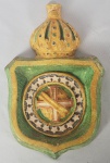 IMPÉRIO DO BRASIL - ESCUDO DO IMPÉRIO BRASEILRO EM FAIANÇA POLICROMADA. ESFERA ARMILAR COM CRUZ  DE  MALTA E 19 ESTRELAS. O ESCUDO ESTÁ SOB COROA IMPERIAL. ASSINADO NA FACE OPOSTA. ITALIA, SEC. XIX. 24 CM DE ALTURA