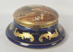 SEVRES - LINDA CAIXA EM PORCELANA DE SEVRES COM CORPO AZUL COBALTO REMATADO POR PLUMAS EM OURO. TAMPA TEM RESERVA COM CENAS DE PÓVOA, LAGO , PERSONAGENS E CAVALEIRO. MARCAS DA MANUFATURA SOB A BASE. FRANÇA, INICIO DO SEC. XX. 20 CM DE DIAMETRO