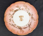 EUFRASIA TEIXEIRA LEITE  MAGNIFICO PRATO FUNDO EM PORCELANA DA MANUFATURA DE THEODORE HAVILAND DEC. DE 1910. BORDA SALMÃO DEGRADE REALÇADA A OURO COM REQUINTADA ABA COM FLORES E RAMAGENS. CALDEIRA COM MONOGRAMA TL ENTRELAÇADO. PERTENCEU A EUFRÁSIA TEIXEIRA LEITE UMA DAS BRASILEIRAS MAIS EMPODERADAS DO FINAL DO SEC. XIX DO BRASIL. PROVENIENTE DE ACERVO DA FAMILIA FRANÇA, SEC. XIX. 24 CM DE DIAMETRO. Em 1875 José de Alencar lançou o romance Senhora que se inicia com a seguinte sentença: Há anos raiou no céu fluminense uma nova estrela. Tal frase é o prelúdio para apresentação da heroína Aurélia Camargo, personagem principal dessa obra literária. Vários literatos defendem que Aurélia Camargo, rica, órfã e belíssima foi inspirada em EUFRÁSIA TEIXEIRA LEITE (vide retrato nas imagens extras desse lote), neta dos Barões de Itambé e sobrinha do Barão de Aiuruoca. Alencar continua sua descrição com os seguintes adjetivos: Era rica e formosa. Duas opulências, que se realçam como a flor em vaso de alabastro; dois esplendores que se refletem, como o raio de sol no prisma do diamante. A mulher que inspirou o romance foi uma das mais fortes personagens femininas do sec. XIX. Chocou a sociedade quando ficou órfã e partiu para Paris sozinha com sua irmã para fugir da pressão dos familiares que a desejavam casar com um parente para gerir a enorme fortuna herdada dos pais. A influência econômica e política das famílias cafeeiras de Vassouras estendia-se pela região do Vale do Paraíba. Não raro, membros dessas famílias se uniam em verdadeiros casamentos dinásticos, que embaralhavam a ordem dos sobrenomes, mas multiplicavam terras e riquezas. A renda desses clãs cresceu, influenciando na importância política que alcançaram no Império. Eufrásia pertencia a uma família de barões e de membros do Partido Conservador. A fortuna deixada pelo pai equivalia a 5% do valor arrecadado pelo governo brasileiro com o imposto de exportação no ano de 1872, ou à dotação anual do Imperador D. Pedro II. No navio CHIMBORAZO que a levou para Europa conheceu e enamorou-se de Joaquim Nabuco o abolicionista e viveu com ele uma paixão avassaladora, desembarcaram já noivos. Emancipada, Eufrásia ofereceu sua própria mão em casamento para escanda-lo da família. Natural, um abolicionista inflamado em meio a uma família de barões do café. Em 14 anos o noivado entre os dois foi refeito e desfeito inúmeras vezes, e o casamento não se concretizou jamais. Ao falecer solteira Eufrásia deixou uma fortuna equivalente a 1850 kg de ouro doada para caridade. Essa é apenas uma personagem de uma família que foi uma das mais importantes do Império Brasileiro. Vassouras era conhecida como a cidade dos Barões. O titulo de barão estava reservado, desde aépoca de D. João VI, aos proprietários rurais que se projetavam por sua riqueza, mas não por sua participação nos altos postos do governo. Os títulos mais elevados, como os de conde, marquês, eram concedidos aos indivíduos que compunham a alta burocracia, ou seja, à elite política imperial. Havia a possibilidade de um rico cafeicultor também ser um ministro do Império, mas era caso raro. Três ricas famílias cafeicultoras do município de Vassouras, os Leite Ribeiro, os Werneck e os Avellar, tiveram, no total, dezenove barões e cinco viscondes entre seus membros. Titulares Vassourenses foram: 25 barões, sete viscondes, uma viscondessa, uma condessa e dois marqueses. Em meio a uma população que em 1872 ostentava 39.253 habitantes, incluindo 20.158 escravos e 19.085 pessoas livres, de todas as raças e origens. Fazendas que somavam quinhentos milhões de pés de café que respondiam 65% de todo café produzido no Brasil.