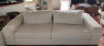 Sofá para 2 lugares, estofado em tecido linhão na cor bege, no estilo moderno, com almofadas presas e encosto com 2 almofadas soltas. Mede 190 cm de comprimento x 94 cm de profundidade do braço e 60 cm de altura.
