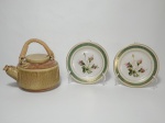 Três itens, sendo: 1 chaleira em cerâmica com alça revestida em palha natural, medindo 18 cm de altura incluindo a alça e 2 pratos pequenos em porcelana decorados com motivos de flores, borda com faixa na cor verde, contorno em dourado, medindo 16 cm de diâmetro.