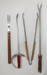 Quatro itens para churrasco, sendo 1 garfo grande com cabo de madeira da marca TRAMONTINA, em aço inoxidável; 1 garfo com pega no formato de espada, marcado IMAGINARIUM em aço inoxidável; 1 espátula em aço inoxidável medindo 67 cm de comprimento e 1 pegador em aço inoxidável com detalhe em madeira medindo 50 cm de comprimento.