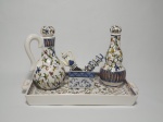 Seis itens, 1 bandeja, 1 porta-azeite, 1 porta-vinagre em cerâmica pintadas à mão, decoradas com motivos florais, 2 espátulas para manteiga com cabos decorados com motivos de xícaras e bule e 1 porta chá em porcelana, pintado à mão, VR2000. As peças maiores medem 17 cm de altura (consta bicado na borda do porta vinagre e na bandeja).