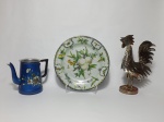 Três peças em metal, sendo 2 com revestimento em ágata. Um prato decorado com motivos de frutas e borboletas, medindo 20 cm de diâmetro; 1 bule em alumínio sem tampa, pintado na cor azul, decorado com motivo de flores, medindo 15 cm de altura e 1 escultura em metal representando um galo, medindo 28 cm de altura.