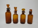 Quatro vidros de Pharmacia, na cor âmbar, de tamanhos diferentes e tampas com formatos diferentes.