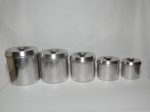 Jogo de 5 potes em alumínio com tampas, para mantimentos, sendo que o maior mede 20 cm de diâmetro x 18 cm de altura, todos no formato cilíndrico, com pegas em plástico rígido na cor preta.