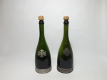 Duas garrafas de bebida (vinho) em vidro verde com guarnições em metal com desenhos de parreira e escudo do fabricante SEGURA VIUDAS. As garrafas estão vazias, tampa em cortiça, medem 33 cm de altura.