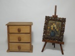 Dois itens em madeira, sendo 1 mini-cômoda composta de 3 gavetas, puxadores em madeira, 17 x 16 x 10cm. 1 quadro exposto no cavalete.