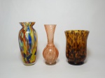 Três vasos de vidro, um no formato bojudo multicolorido, 1 solifleur com pintura iridescente e um vaso mesclado nos tons de marrom. Mede o maior 19 cm de altura.
