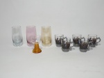 Nove itens em vidro colorido, de modelos, tamanhos e procedências diversos, sendo 3 copos para aperitivo, 1 mini taça para licor e 5 canequinhas para café com alça e suporte em estanho.