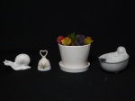 Quatro peças em porcelana, sendo: 1 vaso com suculentas artificiais, medindo 14 cm de diâmetro x 10 cm de altura; 1 saboneteira no formato de banheira na cor branca; 1 escultura no formato de caramujo e 1 sino com a pega no formato de coração. (No sino falta o badalo).