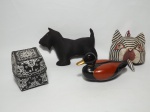 Quatro itens de modelos, materiais e procedências diversos, sendo: 1 caixa de palha decorada com motivos orientais em preto e branco; 1 pato de cerâmica; 1 cachorro feito de tecido na cor preta, representando um Fox Terrier (raça inglesa) e 1 sino de madeira representando a cara de um gato. Medida maior 22 x 14 cm.