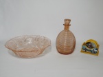 Três itens, 1 licoreira em vidro na cor rosé, medindo 20 cm de altura; 1 centro de mesa em vidro trabalhado com motivo de flores nos tons rosé (apresenta trincado) e 1 kit de porta copos em madeira decorados com lugares do Equador, composto de 6 porta copos e suporte para os mesmos.