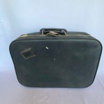 PRIMICIA - Antiga mala de viagem em couro sintético da cor preta com alça com pés em bola e fechadura com chave. Med.: 40cm de altura, 9cm de largura e 50cm de comprimento. Possui desgastes na costura e no ziper. Acompanha chave.