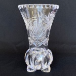 Vaso em cristal translúcido com decorações em formatos geométricos, flores e folhas, com corpo recortado e pés. Med.: 19cm de altura e 11,5cm de diâmetro. Apresenta bicados nos pés e borda; e fundo com rachadura.