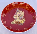 Prato decorativo de pendurar em porcelana branca japonesa com decorações de faisão e flores em dourado sob fundo vermelho. Med.: 16cm de diâmetro.