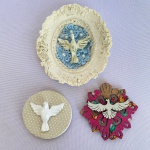 Lote com 3 (três) divinos sendo: Um em resina para parede com decorações de flores e arabescos com 10cm de largura; e Dois imãs para geladeira (um em resina e outro mdf). Med.: 6,5cm e 8cm de diâmetro respectivamente. Divino de mdf está com perda no pano.