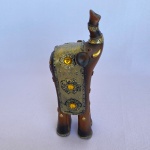 Escultura de elefante em resina na cor marrom com detalhes em dourado e bolas amarelas. Med.: 19cm de altura e 7cm de comprimento.