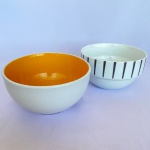 Lote com 2 (dois) bowl de porcelana na cor branca um com bordas decoradas com fitas pretas da marca Kenya e outro com interior na cor de laranja. Med.: 7,5cm de altura e 13cm de diâmetro; e 7,5cm de altura e 14cm de diâmetro.