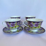 Lote com 4 (quatro) Xícaras com pires em porcelana branca com decoração de flores roxas com fundo verde e roxo e fitas douradas. Med.: Xícara com 7cm de altura e 9,5cm de diâmetro; e pires com 13cm de diâmetro.