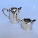 FRACALANZA - Leiteira e cremeira em metal espessurado à prata, alça em voluta, sem tampas med. 10cm e 5cm. Apresenta pouco amassados