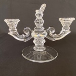 Candelabro em cristal moldado em volutas e figuras geomêtricas com três suportes para velas. Med.: 17cm de altura e 21,5cm de comprimento. Um dos suportes esta quebrado.