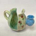 SONHOS DE CERÂMICA - Porta guardanapo em formato de bule vazado em porcelana artesanal com paliteiro embutido. Decorado com cores verdes e rosas. Med.: 10cm de altura e 15cm de largura. Assinado na base. Possui pequeno bicado.