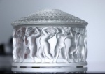 LALIQUE  LES INFANTS CAIXA COM TAMPA 'LES INFANTS ' MODELO CRIADO EM 1931. ASSINADO LALIQUE FRANCE. REPRODUZIDO NO CATALOGO RAIZONNE DO ARTISTA (MARCILHAC, RENE LALIQUE, PARIS 2011, N. 610). A TODA VOLTA DECORADO COM FIGURA DE QUERUBINS DESNUDOS A DANÇAR. TAMPA BELÍSSIMA FORMADA EM PLATEAUS DELIMITADOS POR ANÉIS COM BARRADO DE ROSAS EM RELEVO.EXCELENTE ESTADO DE CONSERVAÇÃO! FRANÇA, SEC. XX. 12 CM DE DIAMETRONOTA:  Reproduzir a emoção do artista através de uma obra de escultura em cristal e jogo de luzes.Artista revolucionário, renomado joalheiro da belle époque, favorito de Sarah Bernhardt, admirado por Gallé, René Lalique desperta extraordinário entusiasmo em todo o mundo apelidado de Rodin das transparências por Maurice Rostand, Lalique soube criar uma arte atemporal e graciosa através de retumbantes sucesso. Excepcional joalheiro e grande mestre do vidro, René Lalique é um dos grandes criadores do art nouveau e do art déco. Desde 1921, a fábrica sediada na Alsácia, região com tradição vidreira, perpetuou o saber artesanal. A mão do homem, artista  artesão da matéria, deixa a sua marca nos objetos e dá-lhes esta força, esta presença tão imaterial: o nosso saber fazer. O estilo Lalique nasce do gesto do artista esboçar um desenho em total osmose com a matéria, um estilo reconhecível pela modelação manual das peças e decorações, à maneira de uma escultura, pela riqueza da decoração figurativa, pelos acabamentos que dão esse contraste característico do cristal transparente e acetinado. Alimentado pela criatividade de uma linhagem de artistas extraordinários, o universo Lalique é rico em know-how que se estende da louça à decoração, da joalharia aos perfumes. Embora a casa Lalique tenha se diversificado em joalheria, arte, decoração de interiores e perfumes, não podemos esquecer que os objetos de decoração em cristal ainda são o principal core business da Lalique. Vasos, xícaras, estatuetas, caixas e garrafas, mas também serviços de vidro constituem a maior parte da produção da fábrica de Wingen-sur-Moder, na Alsácia. Quando decidiu abandonar as joias, René Lalique naturalmente recorreu ao vidro, material que já havia utilizado em algumas de suas joias. Na época, em 1909, alugou a vidraria de Combs-la-Ville e começou a produzir frascos de perfume para grandes perfumistas, depois objetos de decoração. A sua imaginação transbordante leva-o a criar uma grande variedade de objetos: vasos, chávenas, estatuetas, animais, relógios, caixas, garrafas, copos e jarras, que fabrica em vidro na fábrica de vidro de Wingen-sur-moder de 1921.Hoje , Lalique perpetua esta tradição ao publicar em cristal, quer peças originalmente criadas por rené, marc ou marie-claude Lalique, quer peças novas, do atelier de criação interna de Lalique. Assim, todos os anos são criadas duas coleções com mais de dez peças, que nos permitem renovar a nossa oferta aos clientes que adoram Lalique.. Todo o trabalho de Lalique inspira-se em temas caros a René Lalique, nomeadamente a mulher, a fauna e a flora. Além disso, os movimentos artísticos art nouveau e art déco contribuíram largamente para o desenvolvimento de um estilo específico de Lalique. Lalique é acima de tudo a ousada combinação de material e know-how. Graças ao contraste entre a transparência e o cetim, o cristal ganha vida e torna-se expressivo; brinca com sombra e luz e oferece múltiplas possibilidades de tonalidades e relevos. Todos os objetos decorativos, feitos exclusivamente à mão por mestres vidreiros em oficinas na Alsácia, refletem a perfeição do artesanato do cristal.