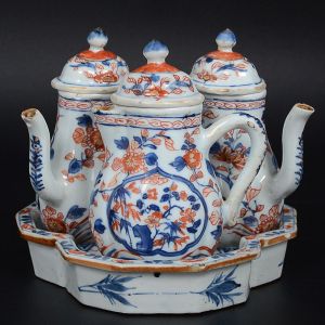 Raríssimo <b>"tête-à-tête"</b> em porcelana Companhia das Índias, decorado em policromia "Chinese Imari", predominando as tonalidades de azul índigo e "rouge de fer" com delicados realces a ouro. Constando de bules p/ chá e café, leiteira e bandeja. Período Kangxi. Circa 1720. Imperceptível bicadinho em uma das tampas. Alt. dos bules 13 cm; Med. da bandeja 16 x 15,5 cm