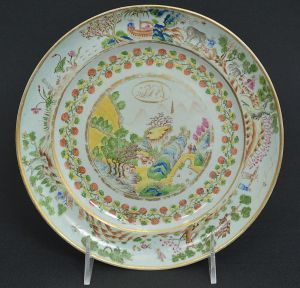 Raro <b>prato menor</b> circular em porcelana Companhia das Índias pertencente ao serviço da Marquesa de Itamarati, Maria Romana Bernardes da Rocha. Na paisagem central, ricamente policromada, observa-se, à esquerda, plantação de café. O tema tem casario tipicamente português e ao fundo, entre as montanhas, observa-se um pagode. Apresenta também uma ponte com dois cidadãos com vestimentas chinesas, que seriam do grupo dos 300 plantadores que vieram para o Rio de Janeiro, plantar, inicialmente chá, e depois café. Circa 1930. Restaurado, e com fio de cabelo. Referências bibliográficas nos mais importantes livros de cerâmica publicados. Diâm. 20 cm