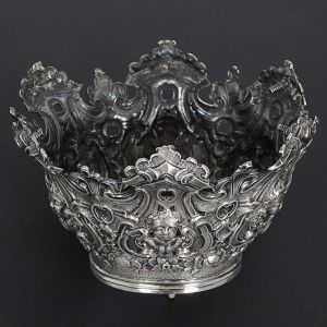 Belíssima <b>coroa sacra</b> em prata brasileira profusamente decorada em repuxados e cinzelados com cabeças de anjos, flores, volutas e acantos em composições barrocas. Séc. XVIII. Alt. 10 cm; Diâm. 15 cm. Peso 350 gramas.