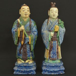 Belíssimo <b>par de estatuetas </b>representando casal de dignatários com seus atributos, em cerâmica chinesa policromada. Requintadas vestes lavradas e pedestal chanfrado decorado com cabeças bizarras. Séc. XVIII. Alt. 54 e 52,5 cm