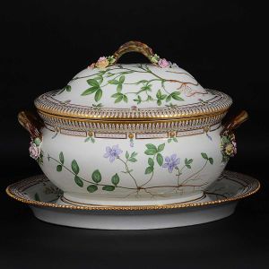 Excepcional grande <b>sopeira com "presentoir"</b> em porcelana dinamarquesa da importante manufatura Royal Copenhagen, modelo <b>"Flora Danica"</b>. Cada peça, inteiramente pintada à mão em belíssima policromia com suas designações botânicas e numeração no verso. Apresentam bordas em mínimos picotados cobertos a folha de ouro. Compr. da sopeira 37 cm. Compr. do "presentoir" 41 cm