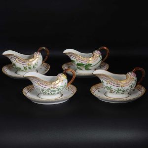 <B>Conjunto de 4 molheiras</b>, "sauce boats", com bases em porcelana dinamarquesa da importante manufatura Royal Copenhagen, modelo <b>"Flora Danica"</b>. Cada peça, inteiramente pintada à mão em belíssima policromia com suas designações botânicas e numeração no verso. Apresentam bordas em mínimos picotados cobertos a folha de ouro. Compr. 23 cm