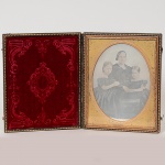 <b>Daguerreótipo</b> sobre vidro colorido, apresentando a Imperatriz Dona Theresa Christina e suas duas filhas, Dona Leopoldina e Dona Isabella. Moldura oval de metal dourado, e montado em caixa retangular de couro marrom com relevo. Circa de 1850. Recibo de aquisição, Galerie Koller, março 1983. Med. 15,5 x 12,5 cm