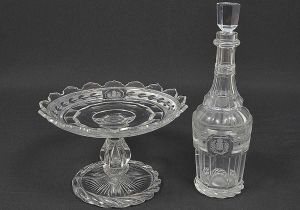 Raríssimo <B>conjunto de fruteira e garrafa</b> em cristal BACCARAT que pertenceram ao Segundo Serviço Imperial. A fruteira apresenta reserva octogonal projetada sobre uma de suas facetas com as armas do Império. O pé termina em torçal. Borda do prato em bicos. A garrafa segue o mesmo padrão decorativo, também trazendo as armas da casa de Bragança. Peças idênticas no Museu Imperial de Petrópolis. A garrafa apresenta mofo. A fruteira apresenta mínimos bicados nas pontas. Alt. da garrafa 31 cm; Alt. da fruteira 15,5 cm; Diâm. da fruteira 23,5 cm