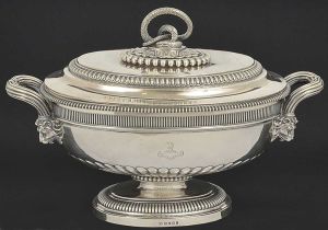<b>PAUL STORR - Belíssima terrina de forma</b> ovalada em prata inglesa George III. Apresenta decoração com faixas em caneluras de diversos tamanhos. Alças frisadas reviradas por flores e implantadas em cabeças de leões. Pega da tampa modelada em serpente sobre folha de acanto rodeada por robusto perolado. Contraste da cidade de Londres de 1806 e marca do prateiro PAUL STORR. Peso 4580 gramas. Compr. 44 cm; Alt. 31 cm