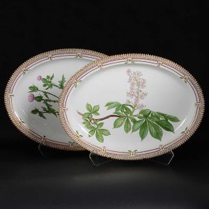 <b>Par de grandes travessas</b> ovais em porcelana dinamarquesa da importante manufatura Royal Copenhagen, modelo "Flora Danica". Cada peça, inteiramente pintada à mão em belíssima policromia com suas designações botânicas e numeração no verso. Apresentam bordas em mínimos picotados cobertos a folha de ouro. Med. 53 x 39 cm