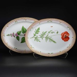 <B>Par de grandes travessas ovais</b> em porcelana dinamarquesa da importante manufatura Royal Copenhagen, modelo <b>"Flora Danica"</b>. Cada peça, inteiramente pintada à mão em belíssima policromia com suas designações botânicas e numeração no verso. Apresentam bordas em mínimos picotados cobertos a folha de ouro. Med. 45,5 x 35 cm