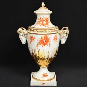 Grande e antigo <b>vaso com tampa</b> em porcelana alemã "Furstenberg". Decoração com ramagens floridas em "rouge de fer" com realces e palmetes a ouro. Pegas laterais modeladas em cabeças de carneiro e pega da tampa terminada em pião. Base quadrada. Marca da manufatura e numeração no verso. Alt. 57 cm