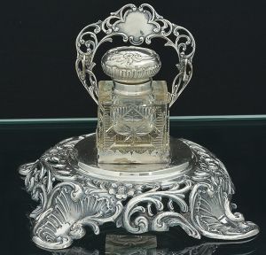 <B>Tinteiro</B> em grosso cristal lapidado com estrelas e frisos. Tampa e suporte em prata portuguesa trabalhada com vazados, flores e volutas. Contraste da cidade do Porto usado de 1886 a 1938 e marca de prateiro. Teor 833 ml. Alt. 14 cm; Compr. 17,5 cm; Larg. 17,5 cm. Peso 200 gramas.
