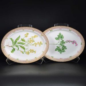 <b>Par de travessas ovais </b>em porcelana dinamarquesa da importante manufatura Royal Copenhagen, modelo <b>"Flora Danica"</b>. Cada peça, inteiramente pintada à mão em belíssima policromia com suas designações botânicas e numeração no verso. Apresenta borda em mínimos picotados cobertos a folha de ouro. Med. 40 x 31,5 cm